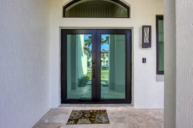 Black-framed impact double doors with an arched transom above, set in a white stucco wall over travertine paving.