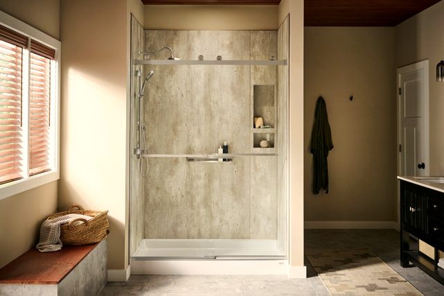 Walk-in shower lined in concrete-look panels, with a robe hanging on a hook and a woven basket on the floor.