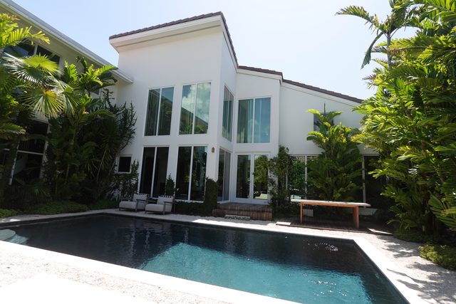Modern white house seen across a dark lap pool, with a double-height glazed wall facing the water.