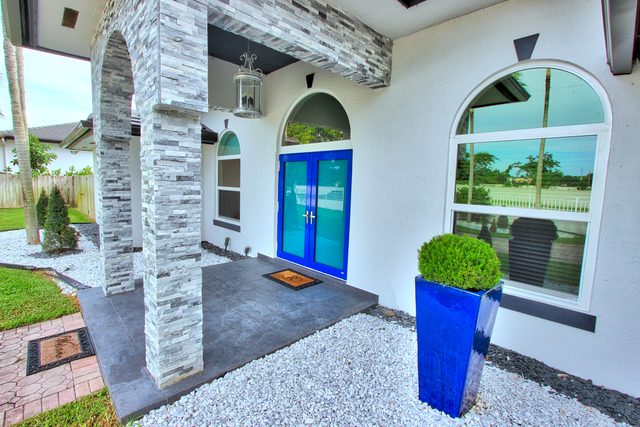 Covered entry with arched stone-clad columns, a tall cobalt planter and white river rock underfoot.