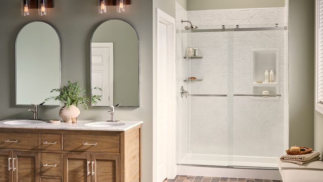 Bathroom with sage green walls, two arched mirrors above a wood double vanity, beside a white shower enclosure.