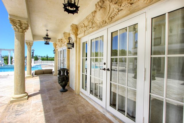 Columned terrace of an estate with carved stone capitals and white French doors, looking out to the pool.