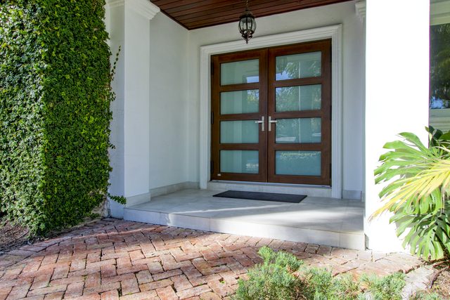 Modern wood entry doors with frosted glass panels, beside a wall covered in ivy above a brick path.