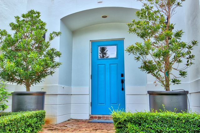 Bright blue front door flanked by two topiary trees in tall planters.