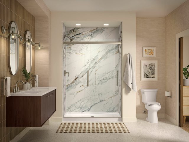 Shower lined in heavily veined marble beside a dark wood floating vanity.